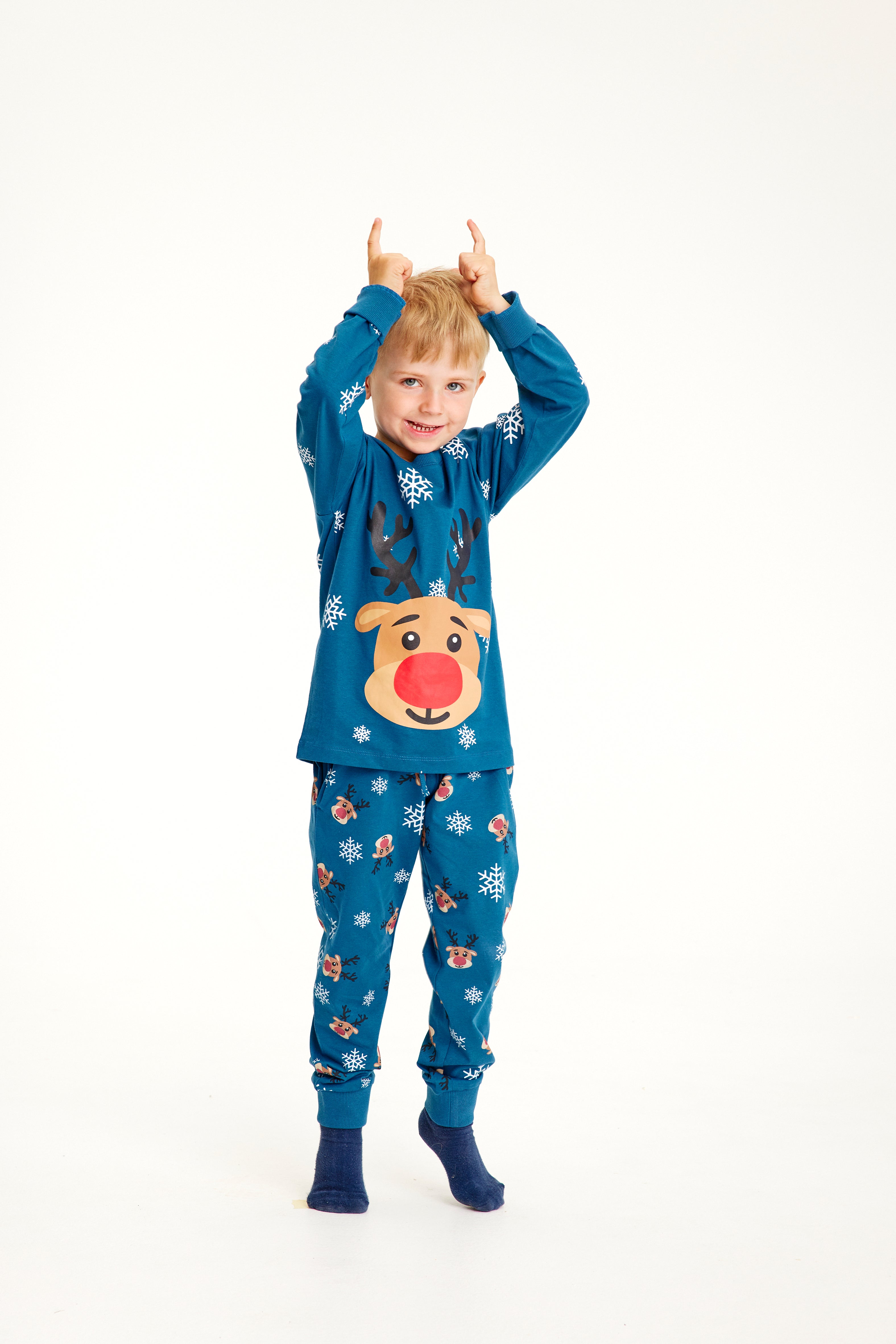 Et barn poserer iført blå julepyjamas med reinsdyr og snøfnugg.